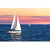 Sailboat sailing towards sunset on a calm evening