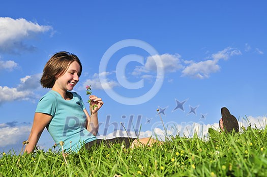 Young teenage girl sitting on grass and smelling a flower