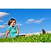 Young teenage girl sitting on grass and smelling a flower