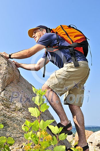 Middle aged man with backpack climbing a rock Middle aged man with backpack climbing a rock