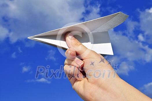 Child's hand holding a paper airplane on blue sky background