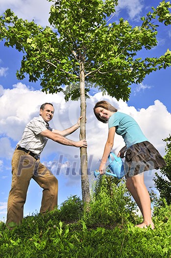 Father and daughter watering a young tree Father and daughter watering a young tree