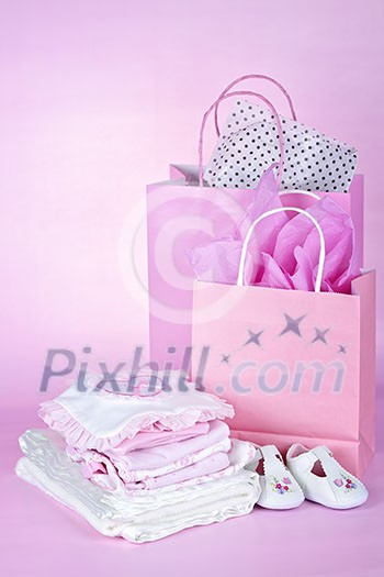 Gift bags and infant clothes for girl baby shower on pink background