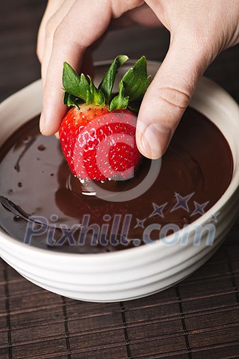 Hand dipping fresh strawberry in melted chocolate