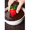 Hand dipping fresh strawberry in melted chocolate