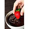 Hand dipping fresh strawberry in melted chocolate