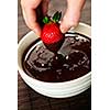 Hand dipping fresh strawberry in melted chocolate