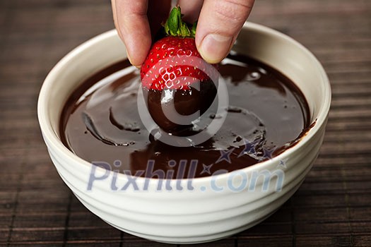 Hand dipping fresh strawberry in melted chocolate