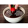 Hand dipping fresh strawberry in melted chocolate