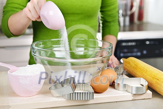 Pouring sugar into mixing bowl with ingredients for making cookies Pouring sugar into mixing bowl with ingredients for making cookies