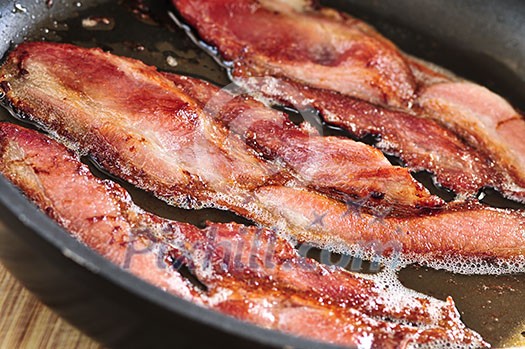 Bacon strips sizzling on a frying pan