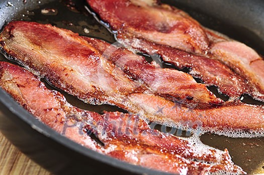 Bacon strips sizzling on a frying pan Bacon strips sizzling on a frying pan