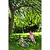 Teenage girl relaxing under green tree with her bicycle