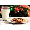 Plate of cookies and glass of milk near Christmas tree