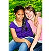 Two teenage girls sitting on grass and hugging