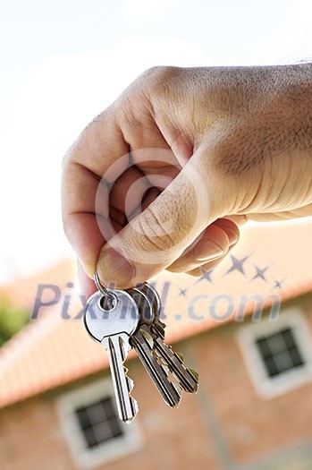 Man's hand holding keys with a house under construction in background Man's hand holding keys with a house under construction in background