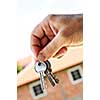 Man's hand holding keys with a house under construction in background