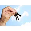 Man's hand holding house keys on blue sky background