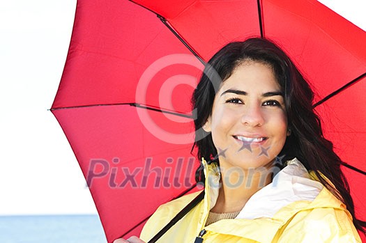 Portrait of beautiful smiling brunette girl wearing yellow raincoat holding red umbrella Portrait of beautiful smiling brunette girl wearing yellow raincoat holding red umbrella