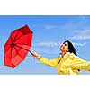 Portrait of beautiful girl wearing yellow raincoat holding red umbrella on windy day