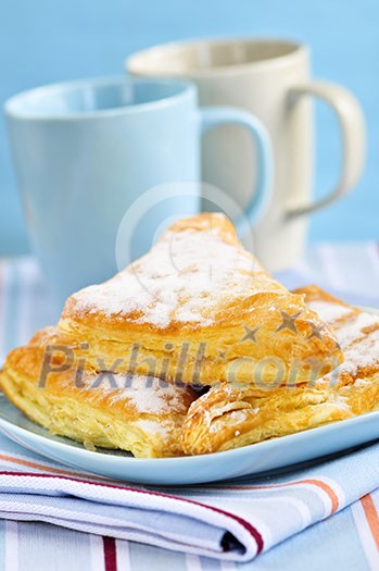 Apple turnovers pastries with coffee cups in the background Apple turnovers pastries with coffee cups in the background