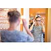 Pretty, young woman choosing new glasses frames in an optician store (color toned image; shallow DOF)