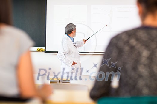 Senior chemistry professor giving a lecture in front of classroom full of students (shallow DOF; color toned image)