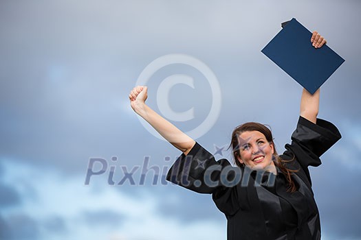 Pretty, young woman celebrating joyfully her graduation - spreading wide her arms, holding her diploma, savouring her success (color toned image; shallow DOF)