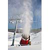 Snow-machine bursting artificial snow  over a skiing slope to alow for the skiing season to start