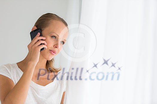 Pretty, young woman calling on her call phone, pensive, concentrating, wearing bright clothes inside a modern, fresh interior (color toned image; shallow DOF)