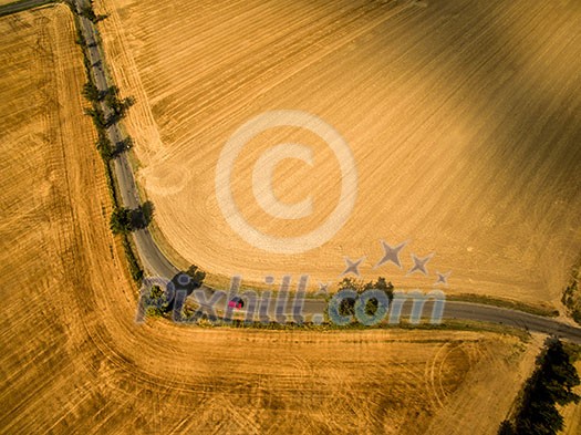 Aerial view of a country road amid fields with a red car Aerial view of a country road amid fields with a red car