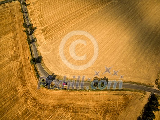 Aerial view of a country road amid fields with a red car