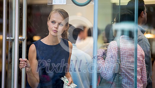 Pretty, young woman leaving a store/restaurant with cash in her hand after having paid for for the goods/food