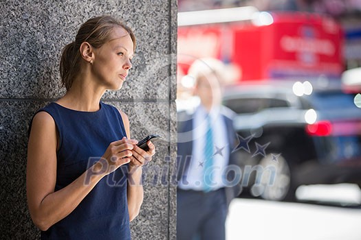 Pretty, young businesswoman talking on the phone in front of a modern building in Manhattan (shallow DOF; color toned image)