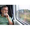Senior man enjoying a train travel - leaving his car at home, he savours the time spent travelling, looks out of the window, has time to admire the landscape passing by
