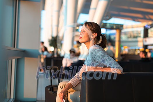 Young female passenger at the airport, waiting for her flight lit by warm evening light, about to check-in