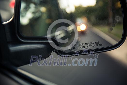 Side rear view mirror of a car on a road with out of focus reflections of the cars behind it (color toned image; shallow DOF) Side rear view mirror of a car on a road with out of focus reflections of the cars behind it (color toned image; shallow DOF)