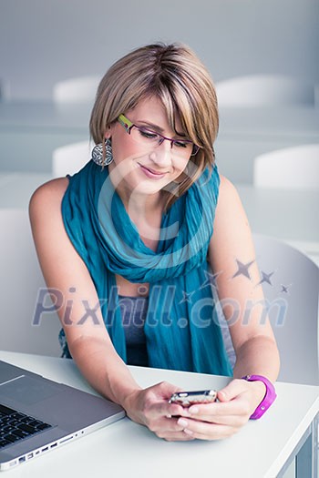 Pretty, young woman at an office, using a laptop and her smartphone