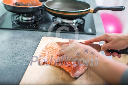 Young woman seasoning a salmon filet in her modern kitchen, preaparing a healthy food