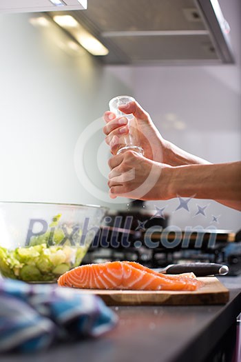 Young woman seasoning a salmon filet in her modern kitchen, preaparing a healthy food Young woman seasoning a salmon filet in her modern kitchen, preaparing a healthy food