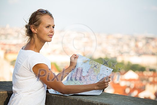 Pretty young female tourist studying a map, enjoying discovering a new city, looking excited (shallow DOF; color toned image)