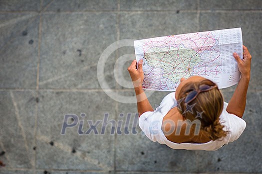 Pretty young female tourist studying a map, enjoying discovering a new city, looking excited (shallow DOF; color toned image)