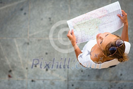 Pretty young female tourist studying a map, enjoying discovering a new city, looking excited (shallow DOF; color toned image)