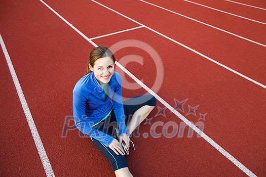 Pretty female runner stretching before her run at a track and field stadium Pretty female runner stretching before her run at a track and field stadium