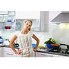 Portrait of a young woman wearing an apron, standing with a confident attitude in her modern kitchen (color toned image; shallow DOF)