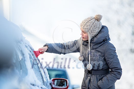 Young woman cleaning her car from snow and frost on a winter morning, she is freezing and needs to get to work Young woman cleaning her car from snow and frost on a winter morning, she is freezing and needs to get to work