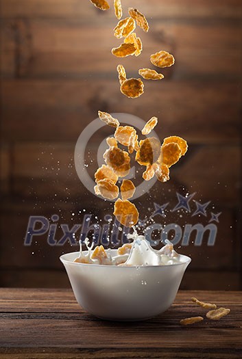 Falling corn flakes with milk splash on wooden background