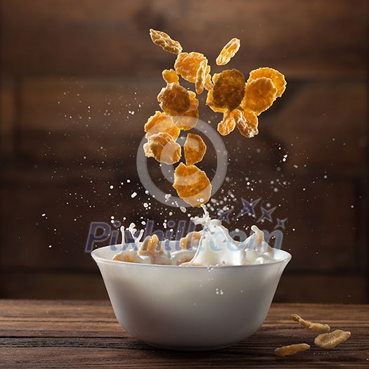 Falling corn flakes with milk splash on wooden background