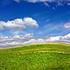 Green field against blue sky and clouds