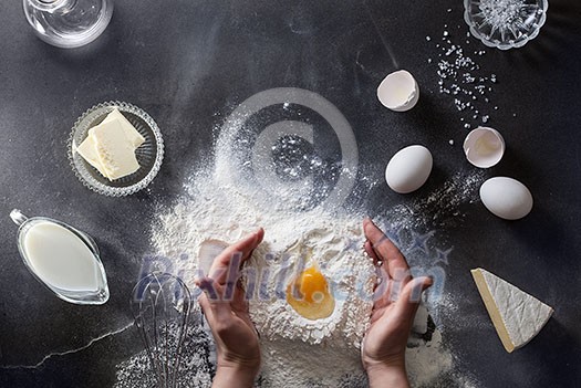 Woman's hands knead dough on table with flour, eggs and ingridients. Top view.